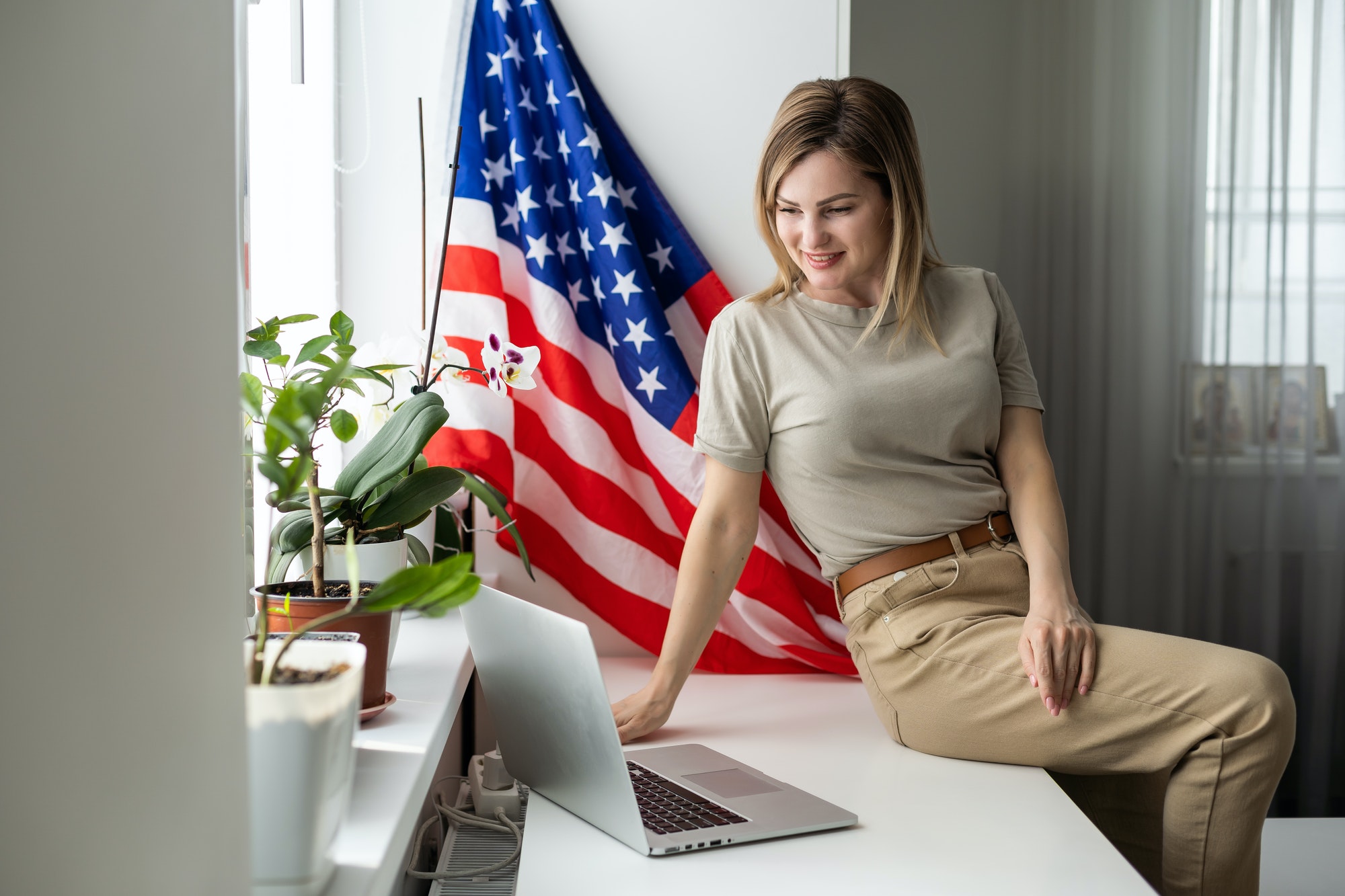 Happy woman employee sitting wrapped in USA flag, shouting for joy in office workplace, celebrating